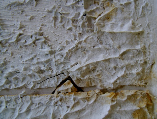 Close-up of a cracked textured wall surface with rough plaster, off-white and cream tones