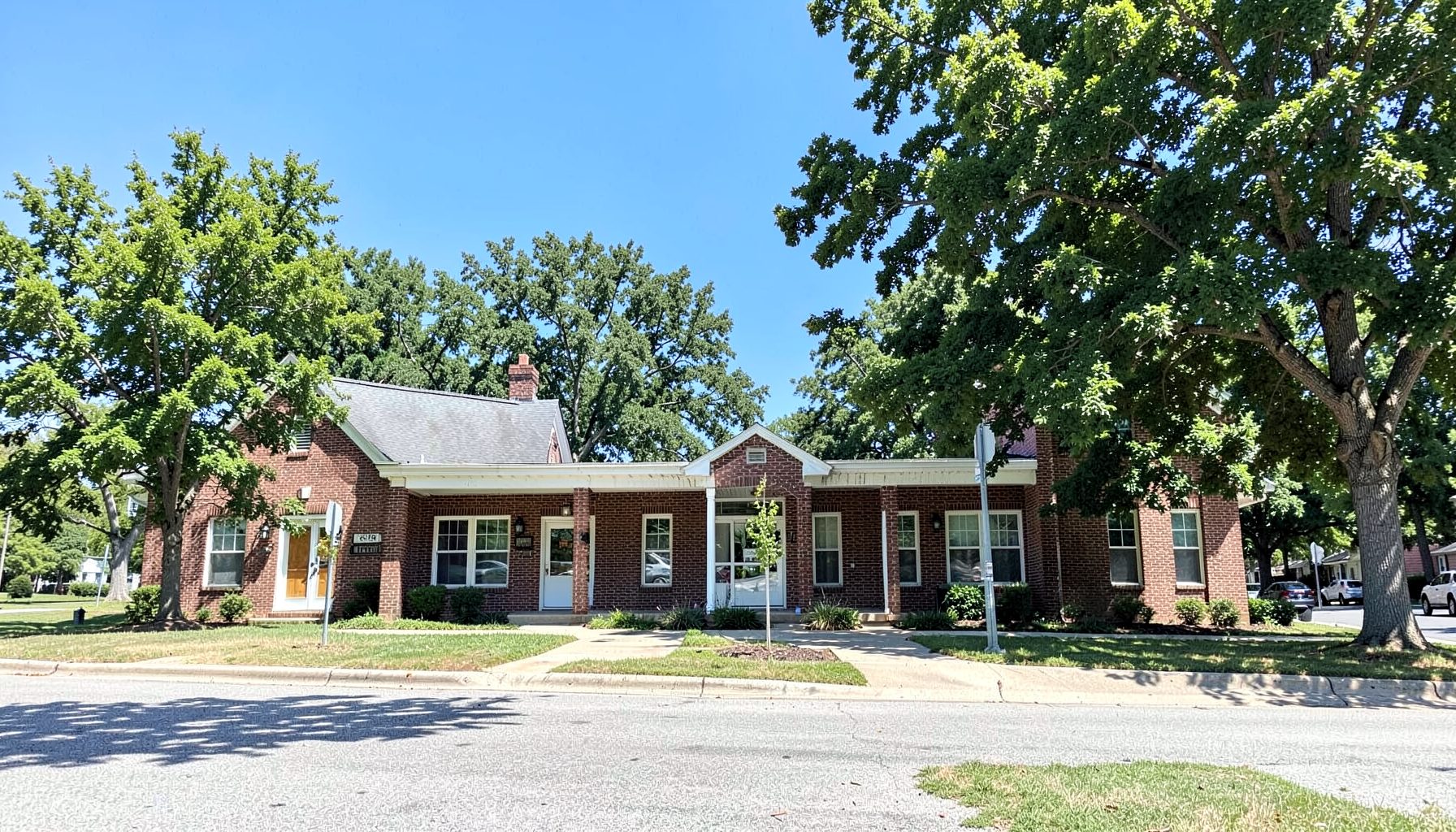 A wide view of a quiet small-town civic building with brick exterior, surrounded by mature trees under a bright blue sky, conveying a calm rural Georgia atmosphere